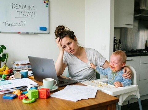 Werkende moeder combineert thuiswerk en zorg voor baby, beeld dat stress en mentale belasting laat zien en het belang van begeleiding en mentale weerbaarheid benadrukt.